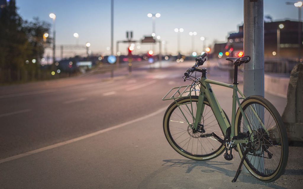 Cykel fastlåst i en lyktstolpe vis en större väg i skymningen.